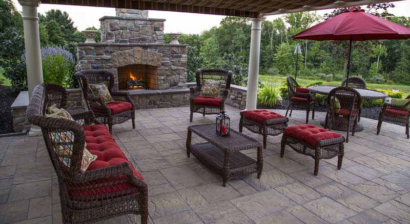 Inviting covered patio with stone fireplace, wicker furniture, and bold red cushions perfect for fall gatherings.