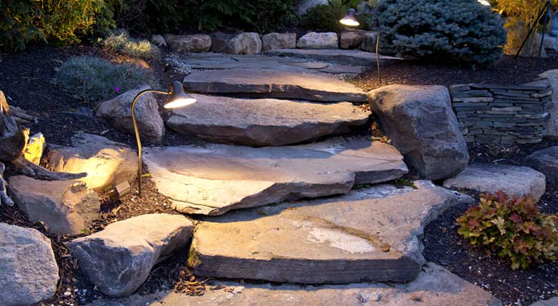 Rustic stone steps with built-in landscape lighting, blending natural rock with functional hardscaping design.