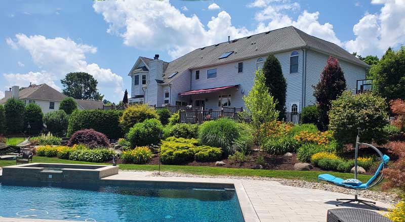 Large backyard landscape design with pool, shrubs, and layered greenery for spring in Morris County NJ.