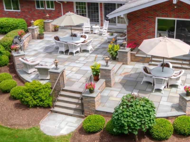 Stone patio with outdoor seating, umbrellas, and garden landscaping