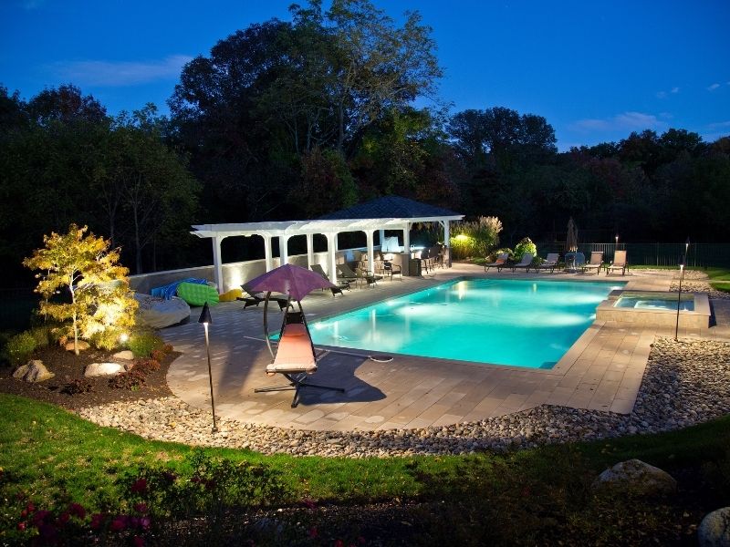 Landscape lighting illuminating a backyard pool and garden at dusk