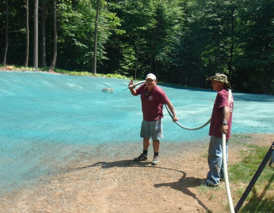 Landscape maintenance workers spraying hydroseed on a sloped area to establish new grass growth