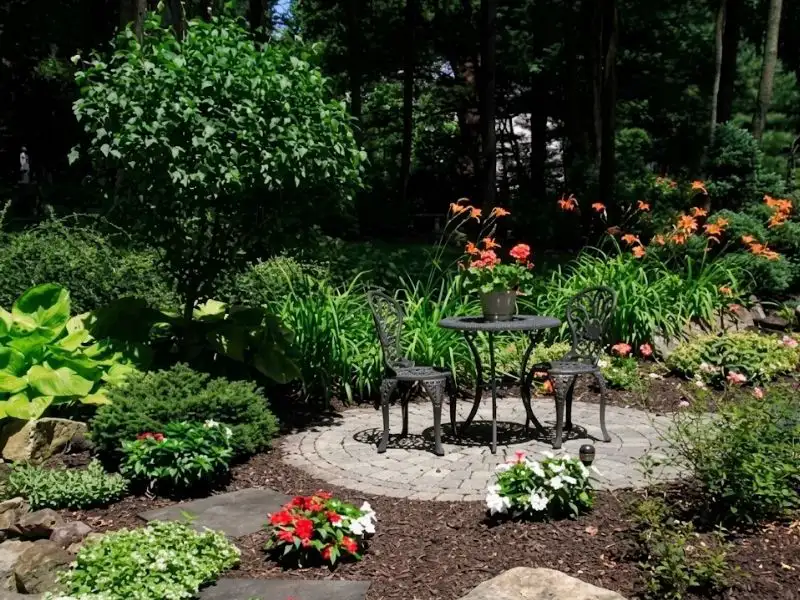 Landscaped garden patio with bistro table, flowering plants, and stone path