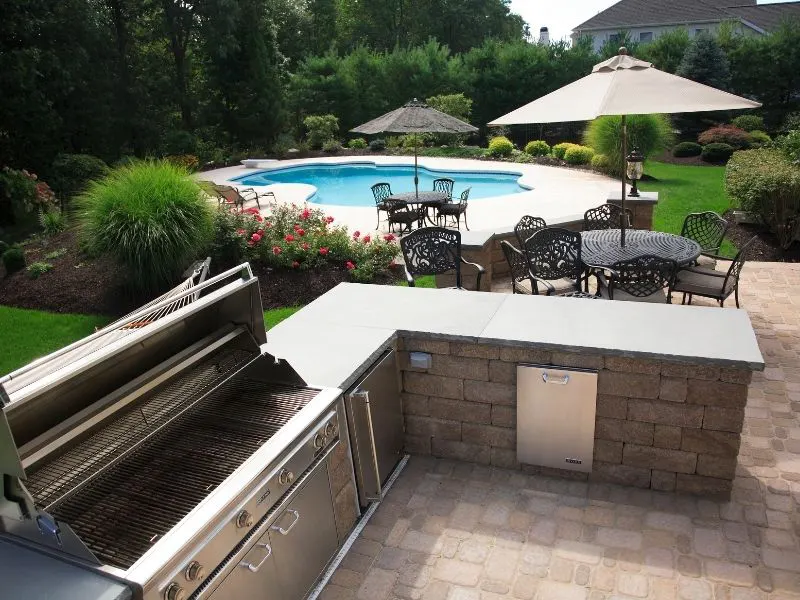 Outdoor kitchen and poolside patio with dining area and landscaped yard