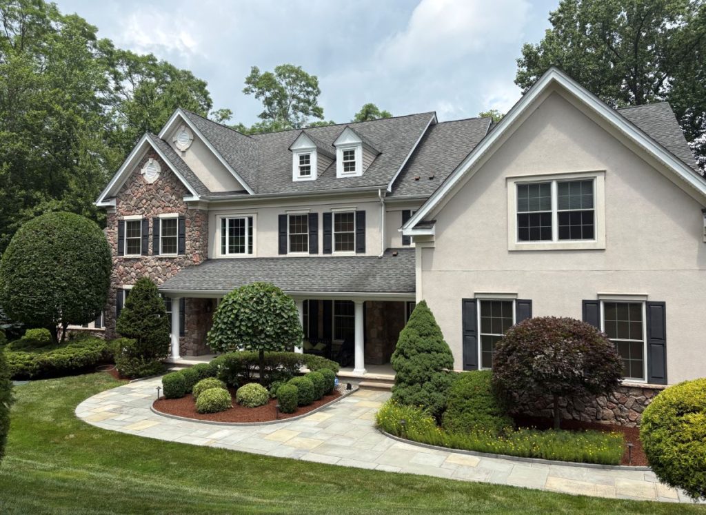 Two-story home with paver walkway, manicured shrubs, ornamental trees, and landscaped front yard